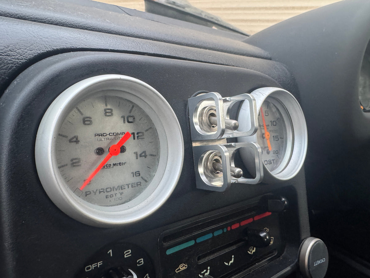 Duskie silver billet aluminium ISS-style toggle switch guard with two switches, mounted next to car gauges.