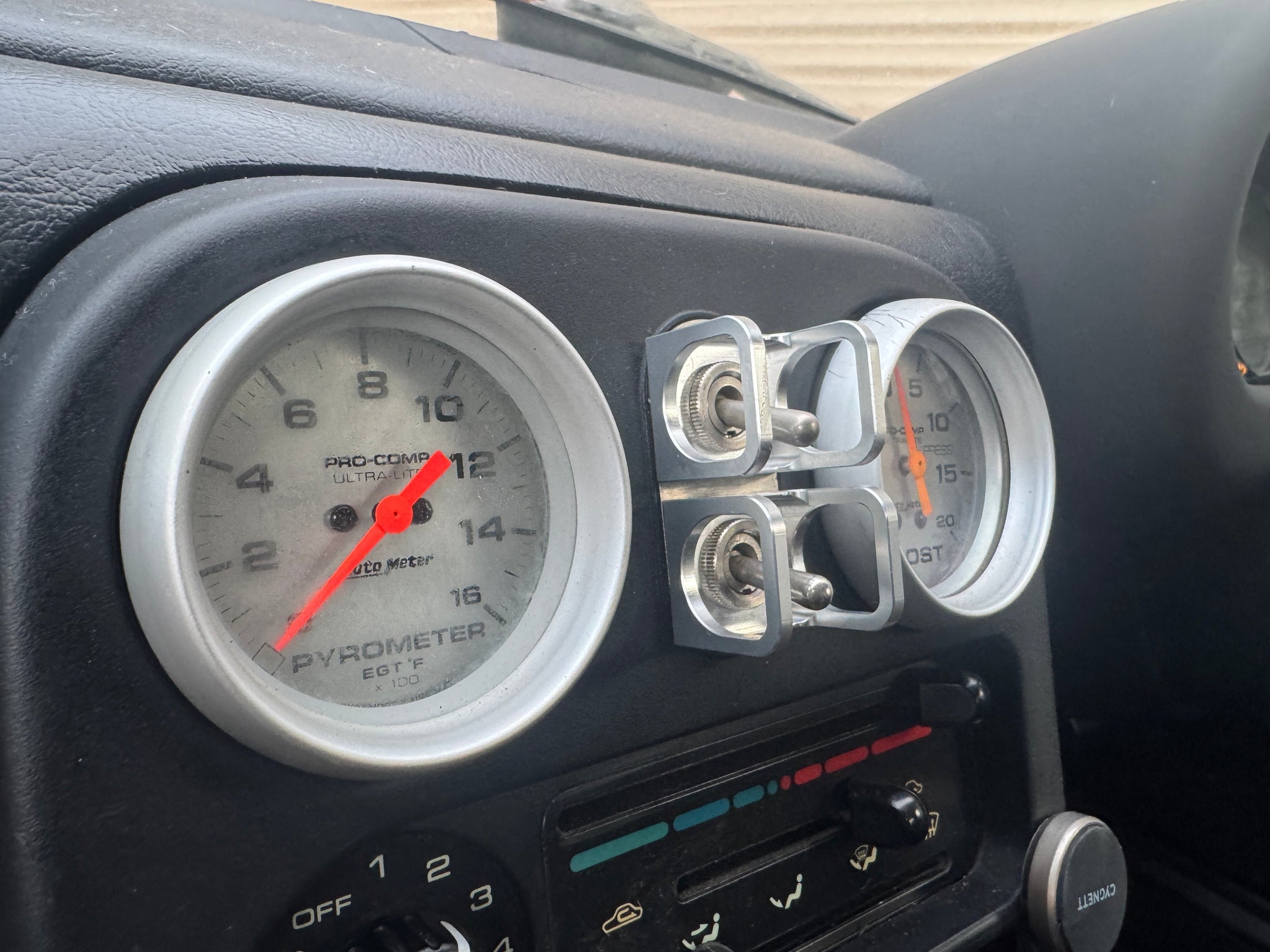 Duskie silver billet aluminium ISS-style toggle switch guard with two switches, mounted next to car gauges.