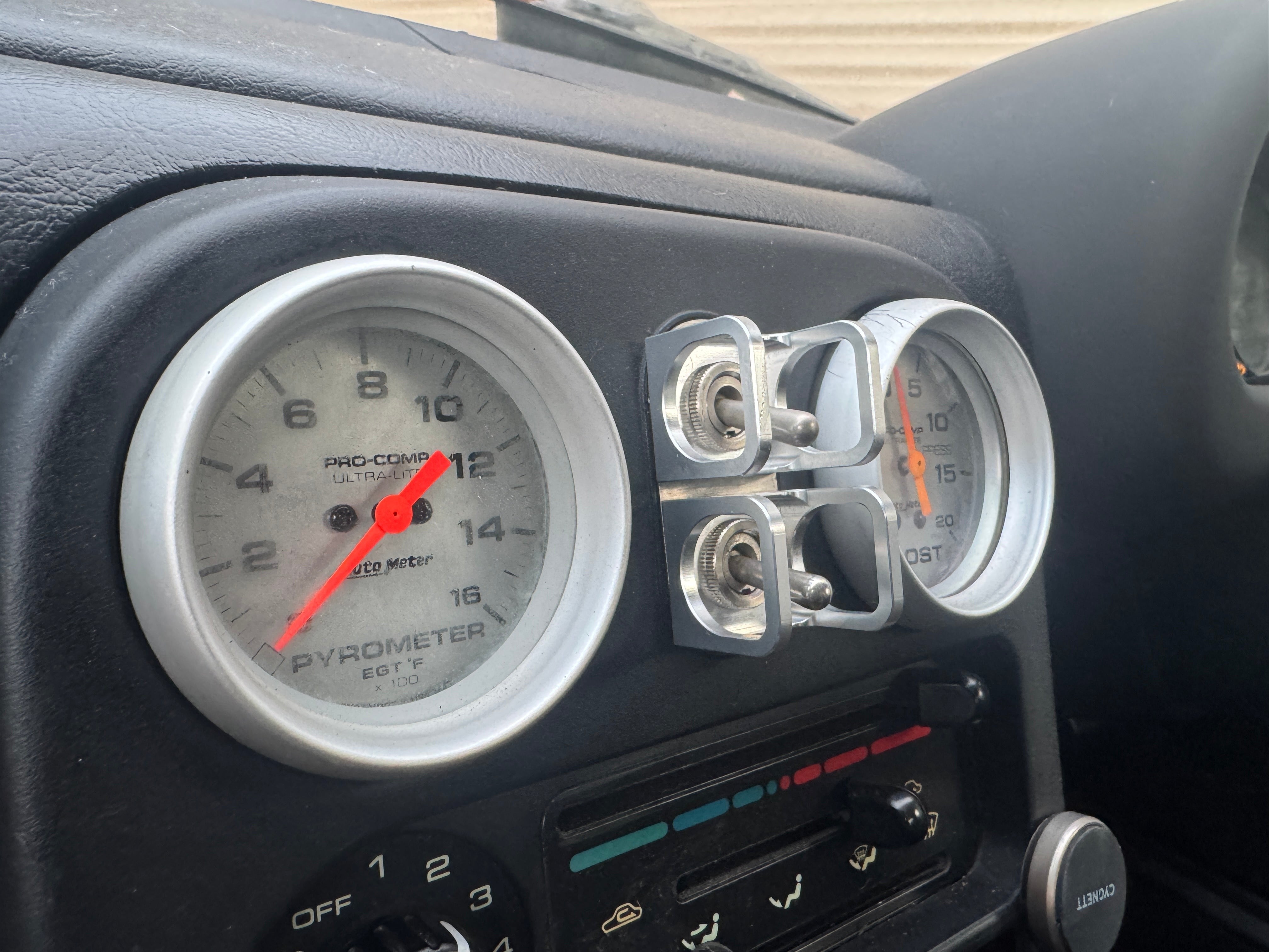 Duskie silver billet aluminium ISS-style toggle switch guard with two switches, mounted next to car gauges.