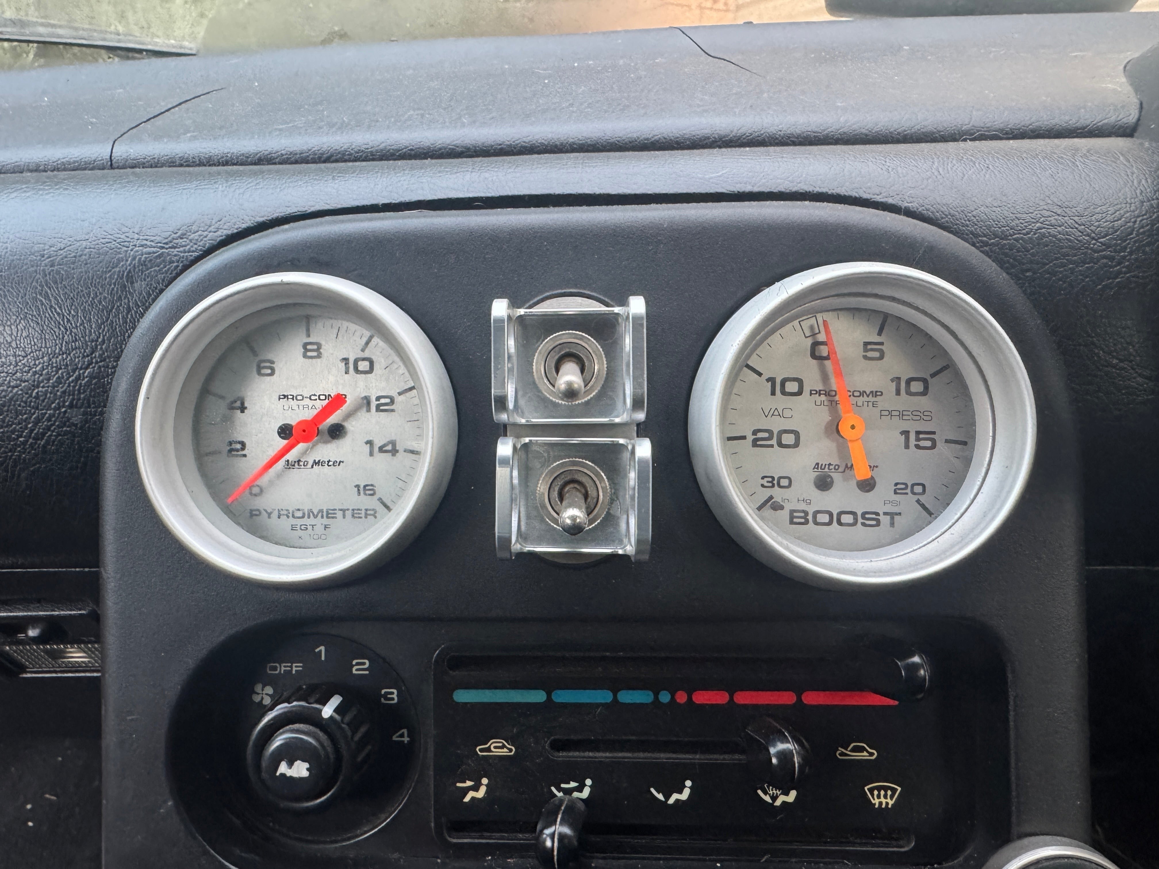 Duskie silver billet aluminum ISS-style toggle switch guard with two silver toggle switches mounted between two gauges on a car dashboard.
